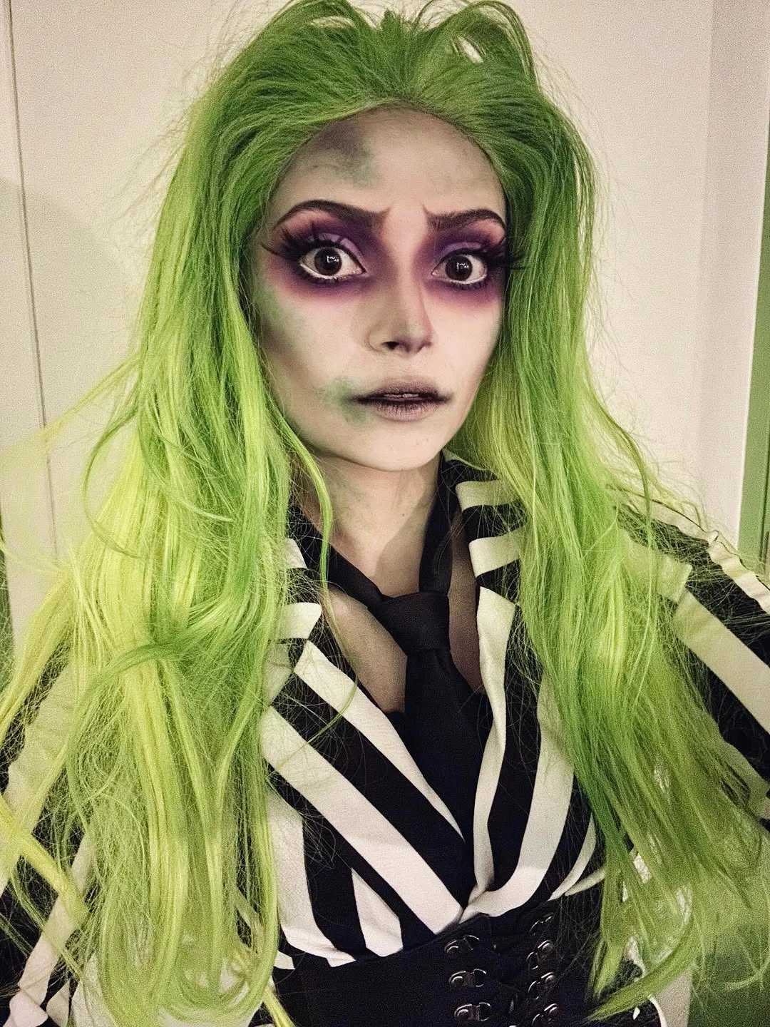 Green wig costume with black-and-white striped top and dramatic dark makeup