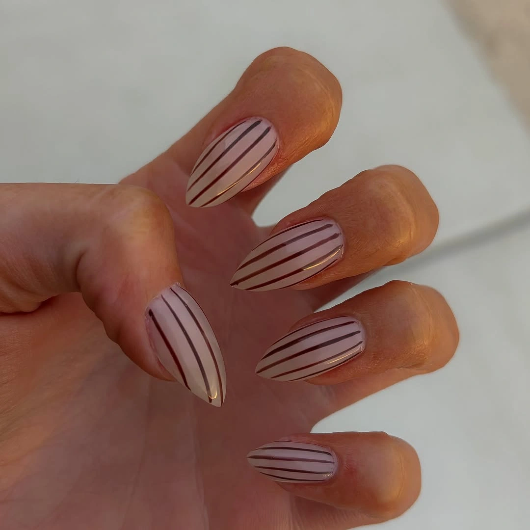 nude almond nails with repeated thin brown stripes