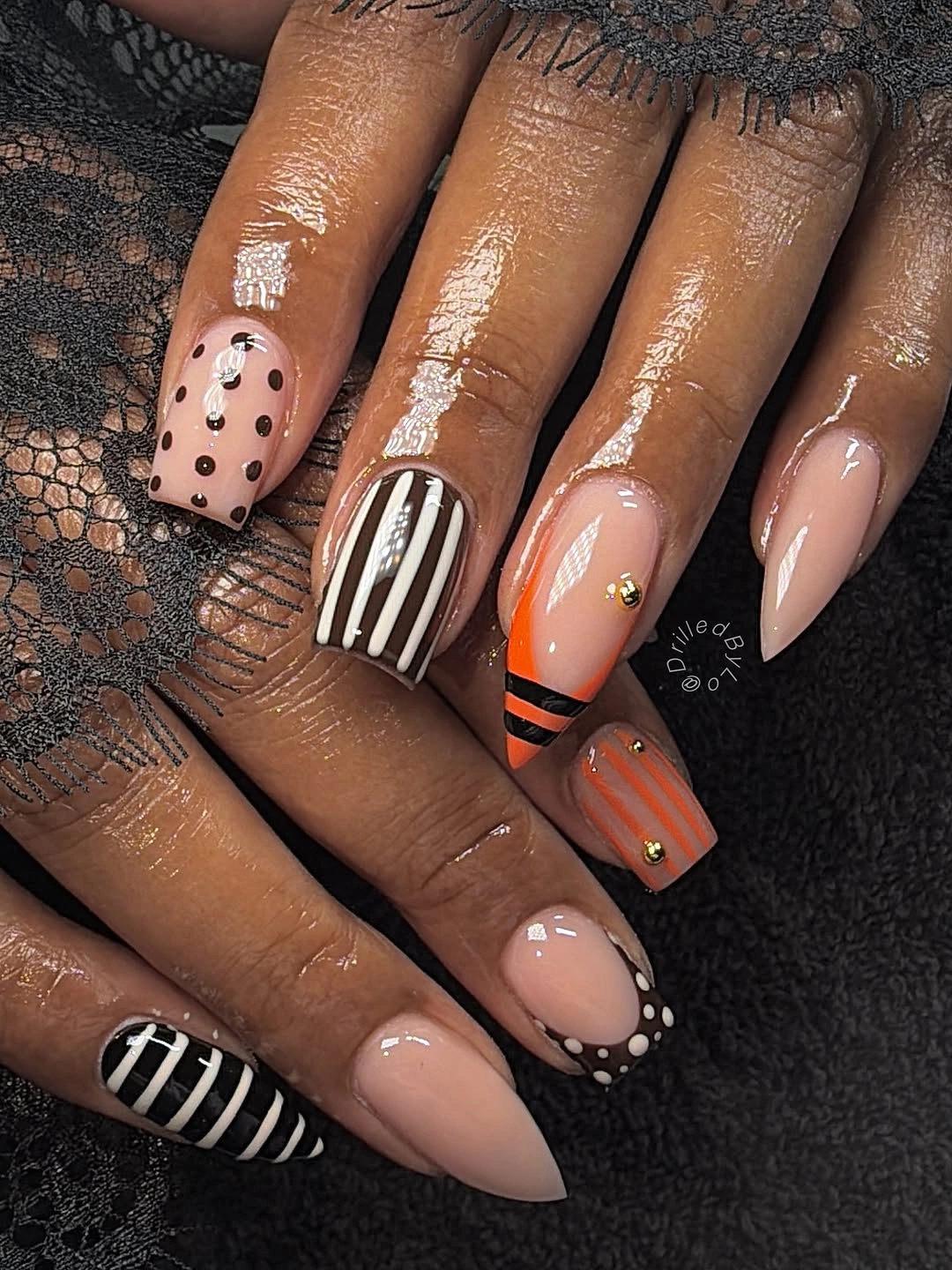 nude almond nails with black white stripes and orange accents
