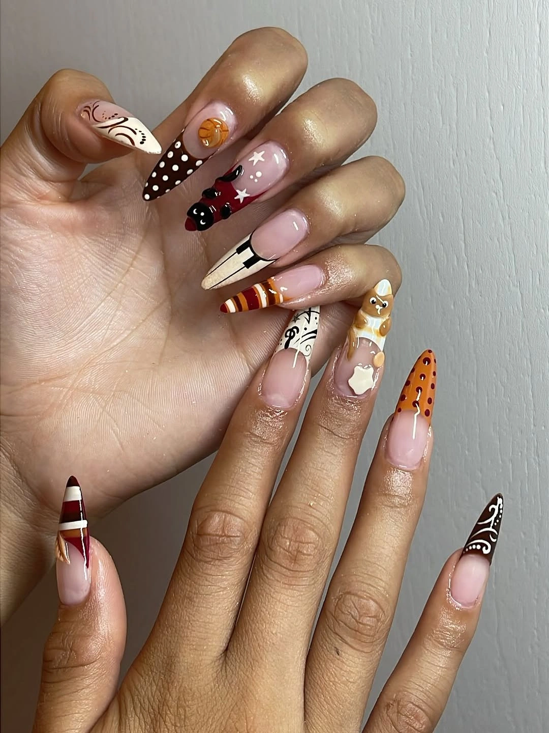 nude square nails with burgundy, orange, striped, and gold accents