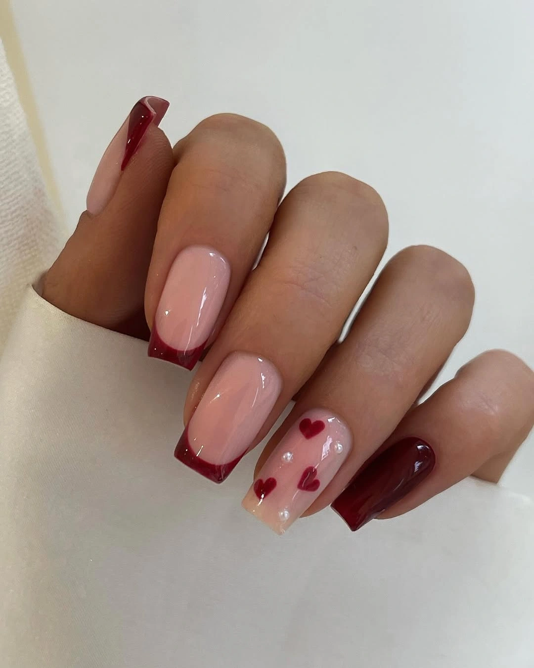 Short burgundy nails with nude panels and tiny hearts