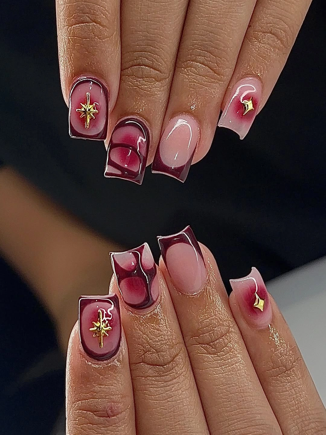 Short burgundy French nails with nude centers and gold stars