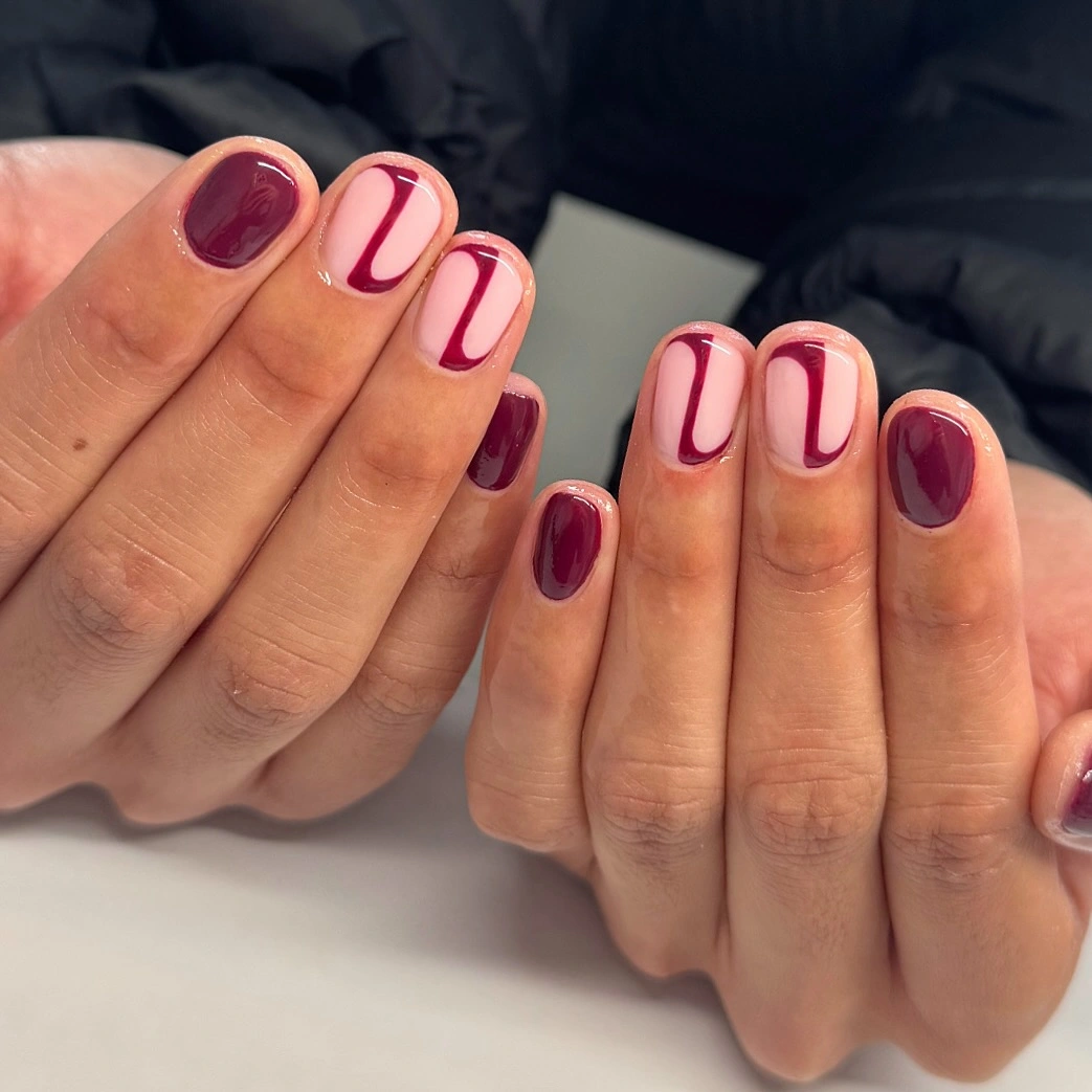Short burgundy nails with nude panels and fine outlines