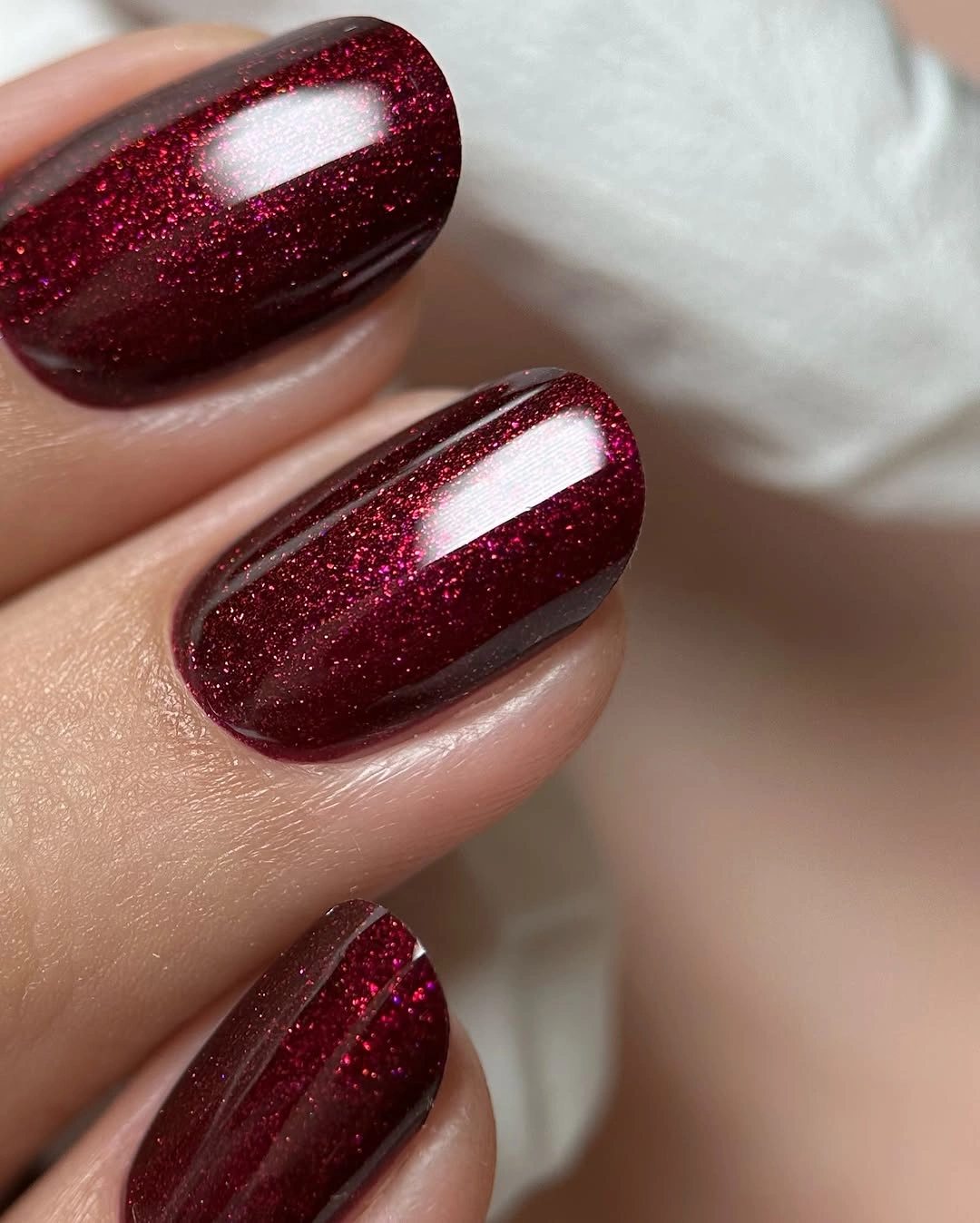 Short rounded burgundy nails with fine red metallic shimmer
