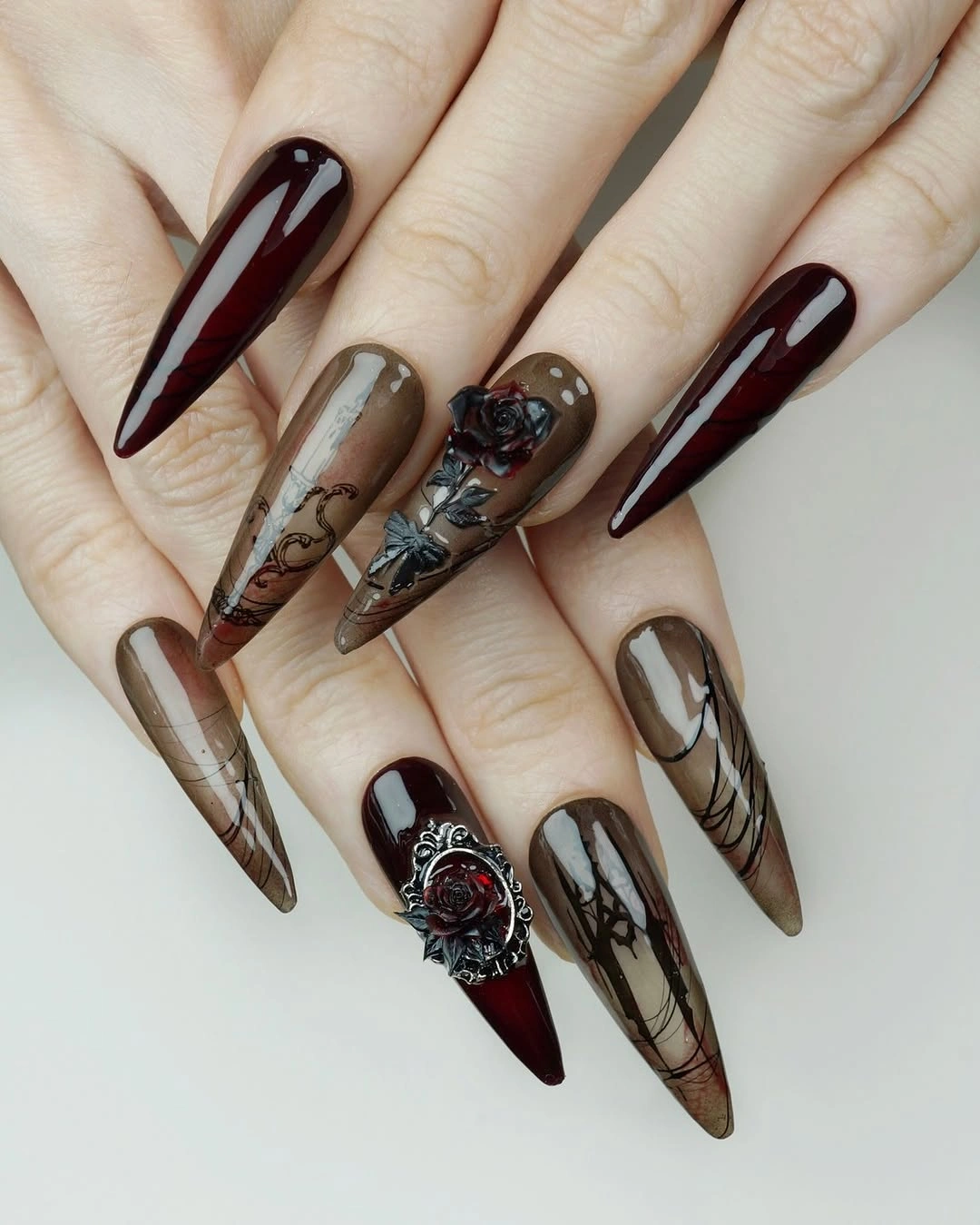Long pointed burgundy nails with smoky panels and ornate accent detail