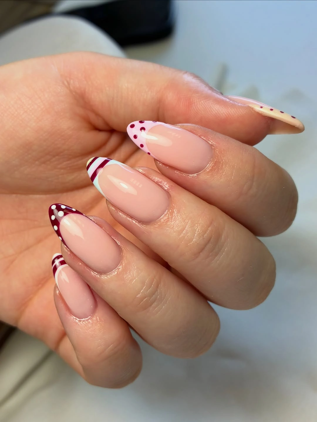 Blush almond nails with narrow burgundy and brown French lines