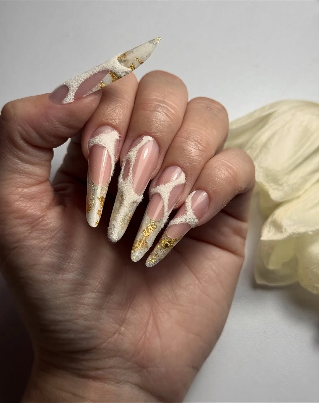 Long stiletto nails with cream swirls and gold tip accents