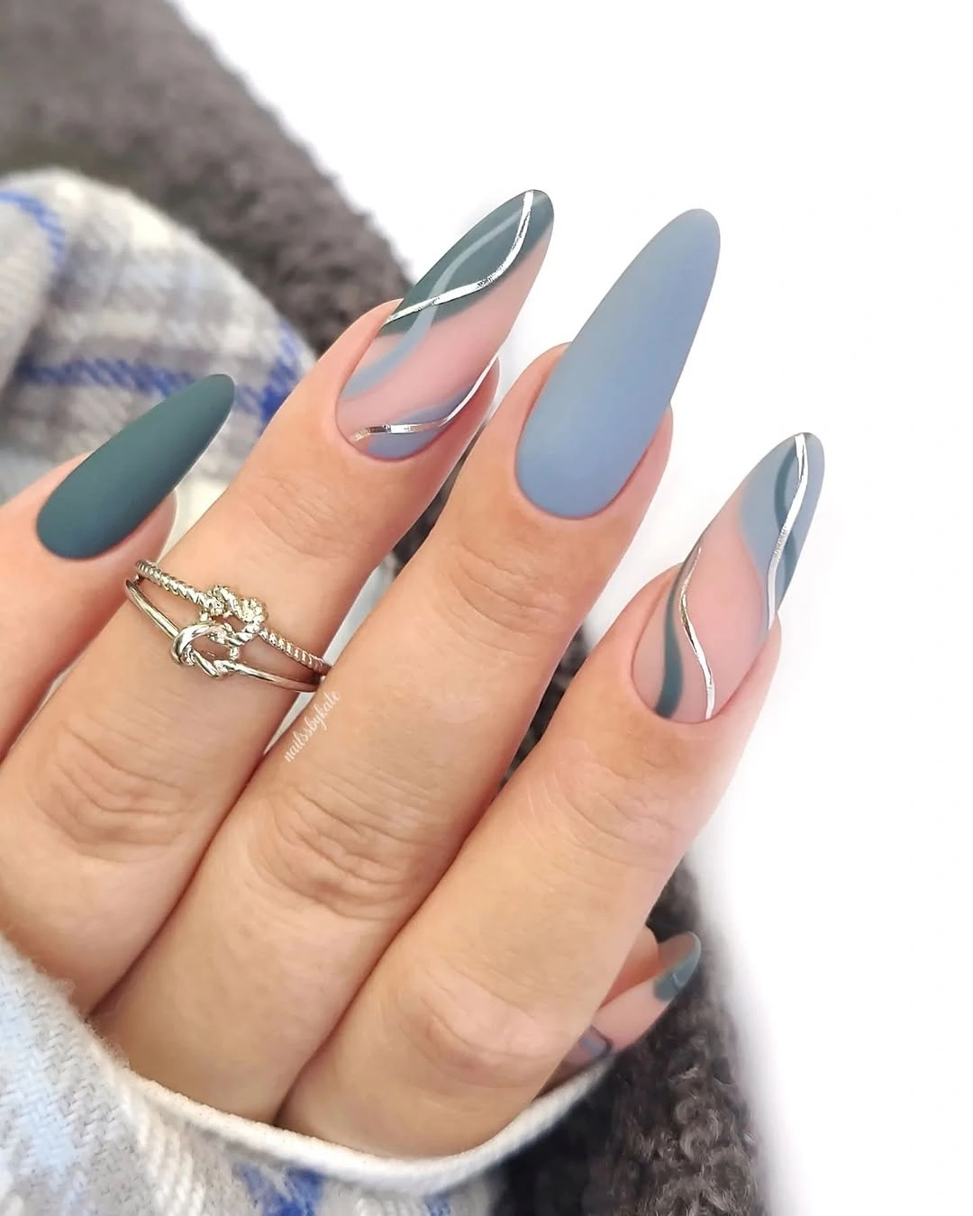 almond manicure mixing matte blue gray, deep teal, nude negative space, and silver wavy lines