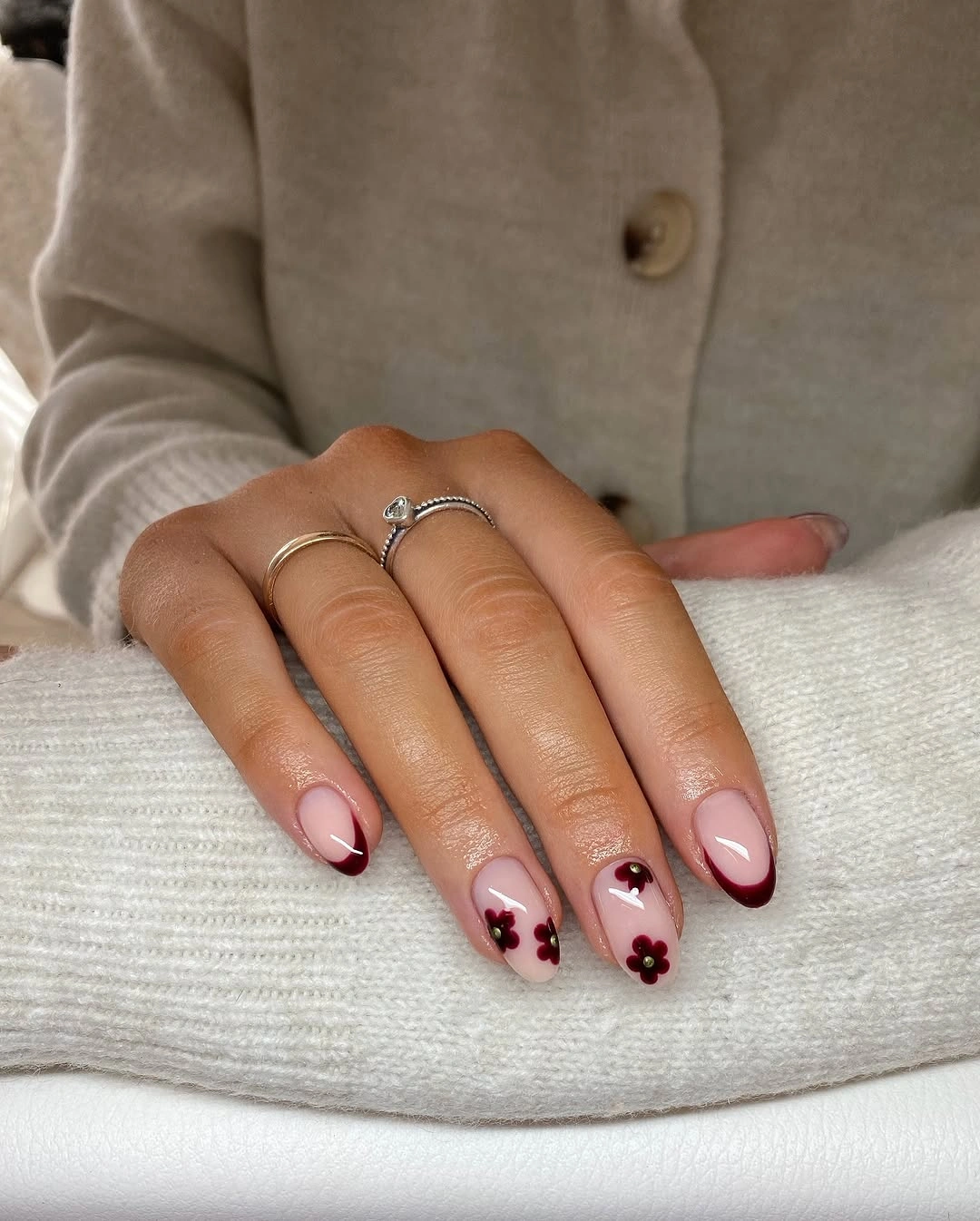 short rounded manicure featuring burgundy French tips and small burgundy flowers on sheer nude nails