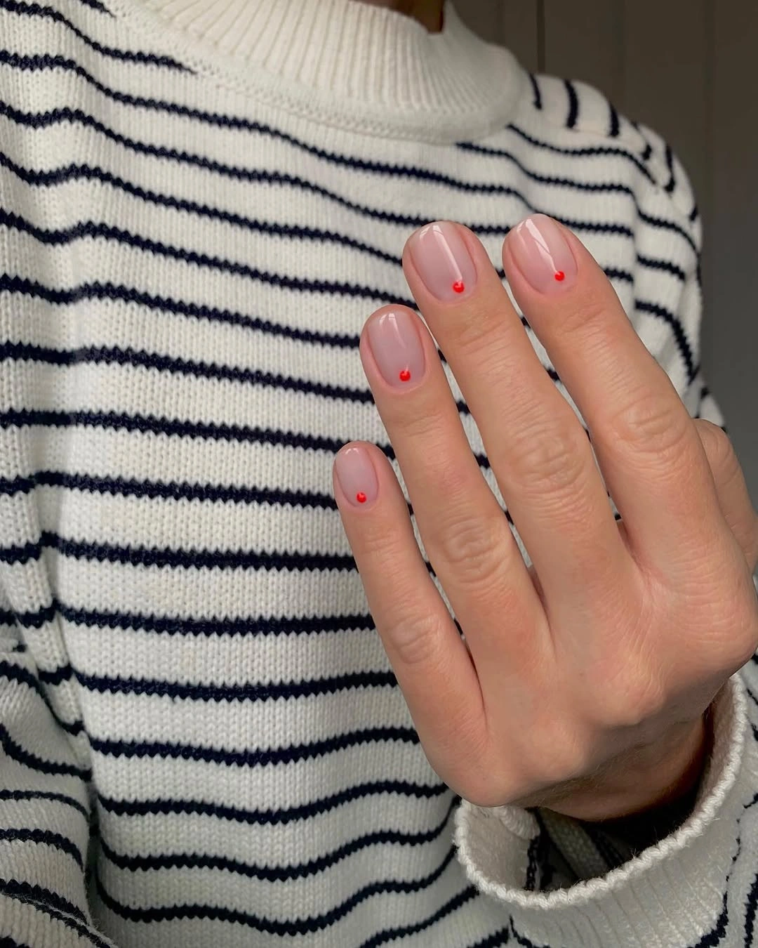 very short natural-looking manicure featuring sheer pink base and tiny red dots near the tips