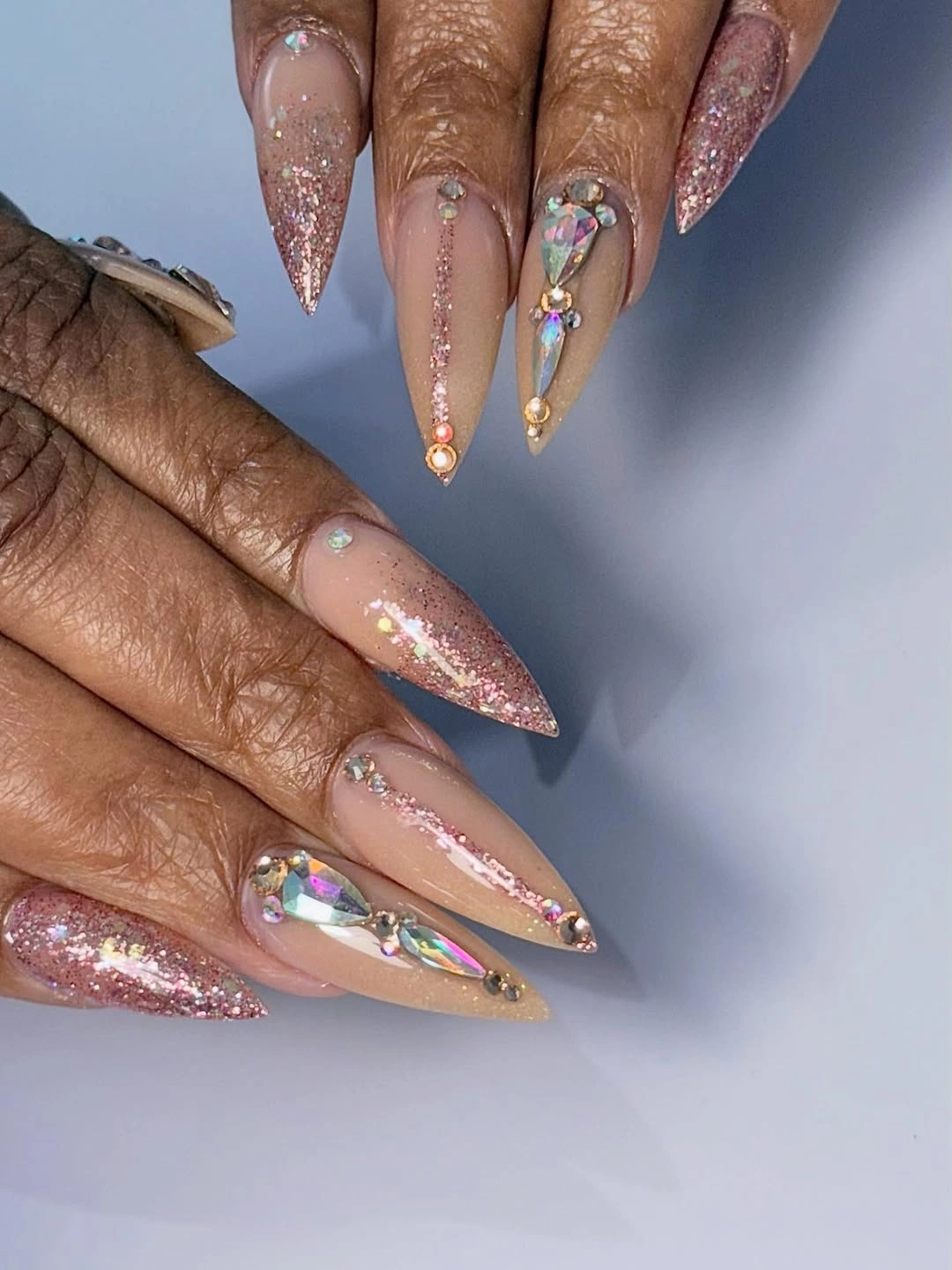 long stiletto manicure featuring nude base, pink glitter fades, rhinestones, and large faceted accents