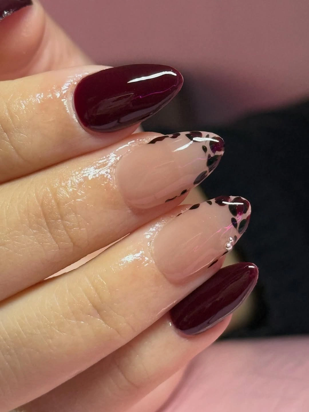 almond manicure featuring glossy burgundy solid nails and nude accent nails with burgundy leopard tips