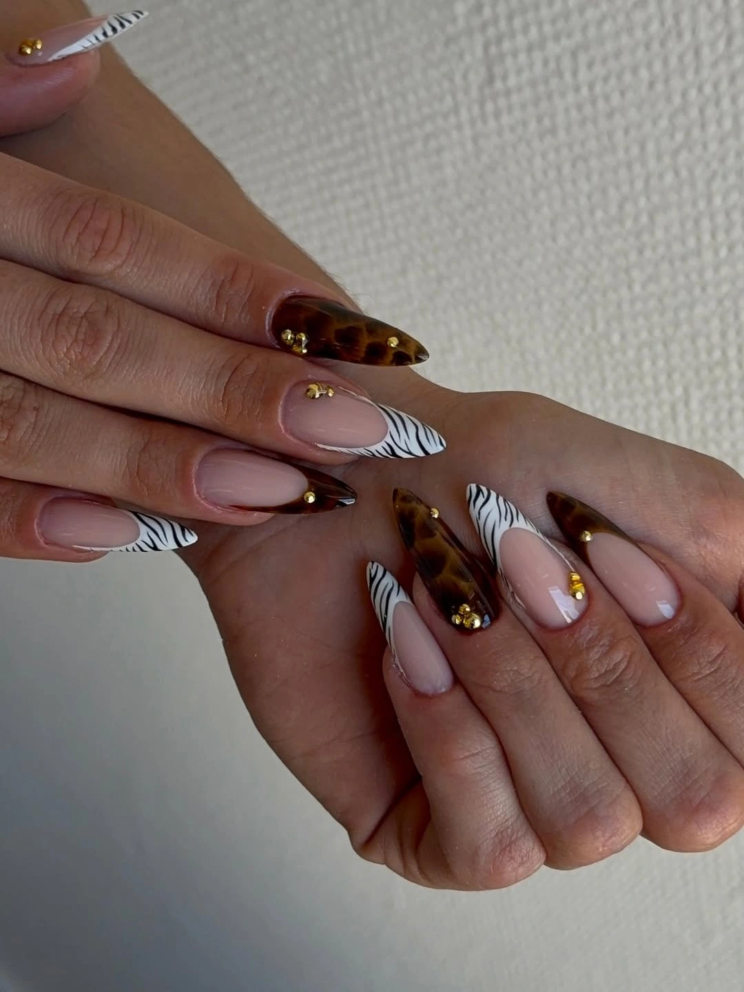 long almond manicure featuring nude bases, tortoiseshell tips, zebra striped tips, and gold studs