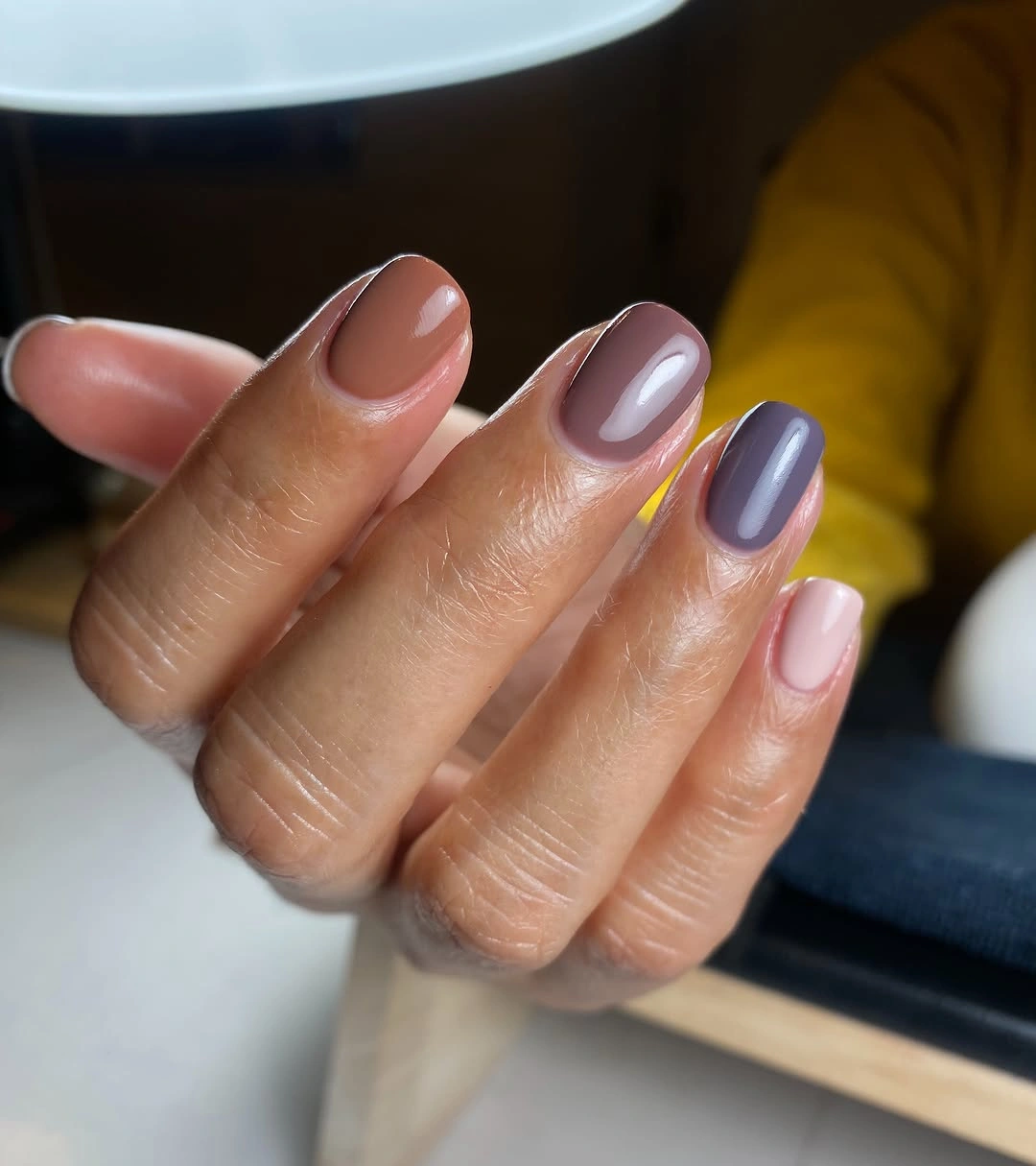 short rounded manicure featuring alternating taupe, mauve-gray, caramel brown, and pale pink glossy colors