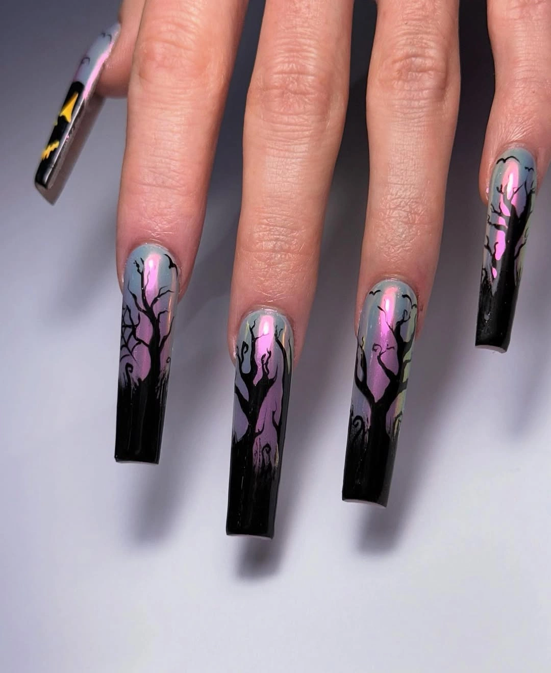 very long coffin manicure featuring black tree silhouettes over gray, pink, and greenish shimmer