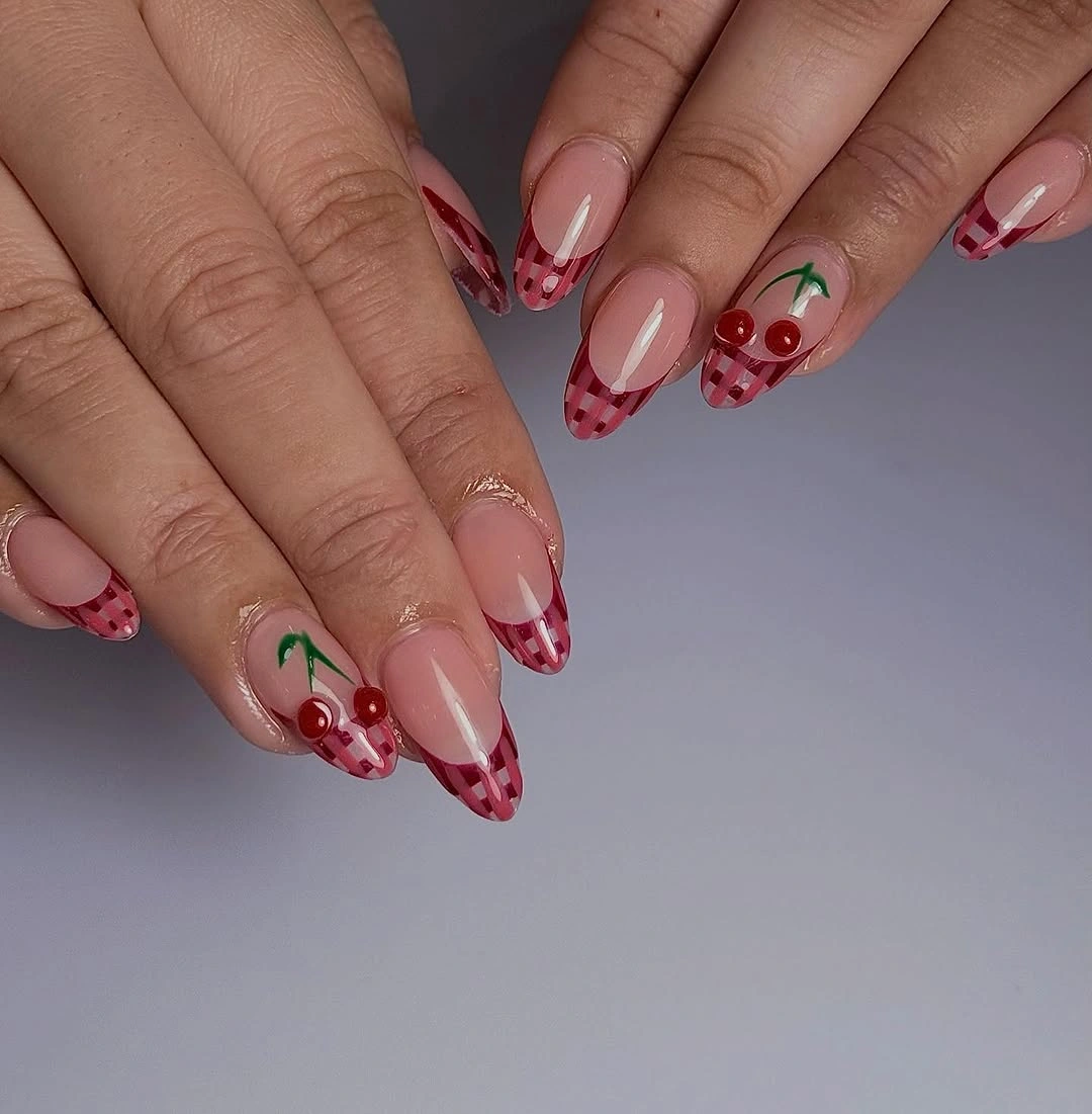 almond manicure featuring red gingham French tips and cherry accents over sheer nude bases