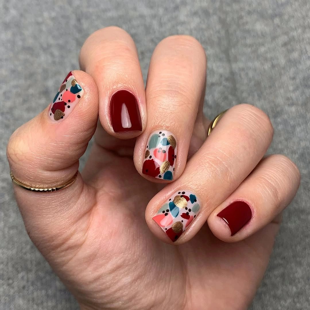 Short rounded red nails with tiny colorful accent details