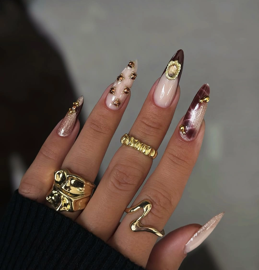 Ornate almond nails with brown shimmer and gold-toned accents
