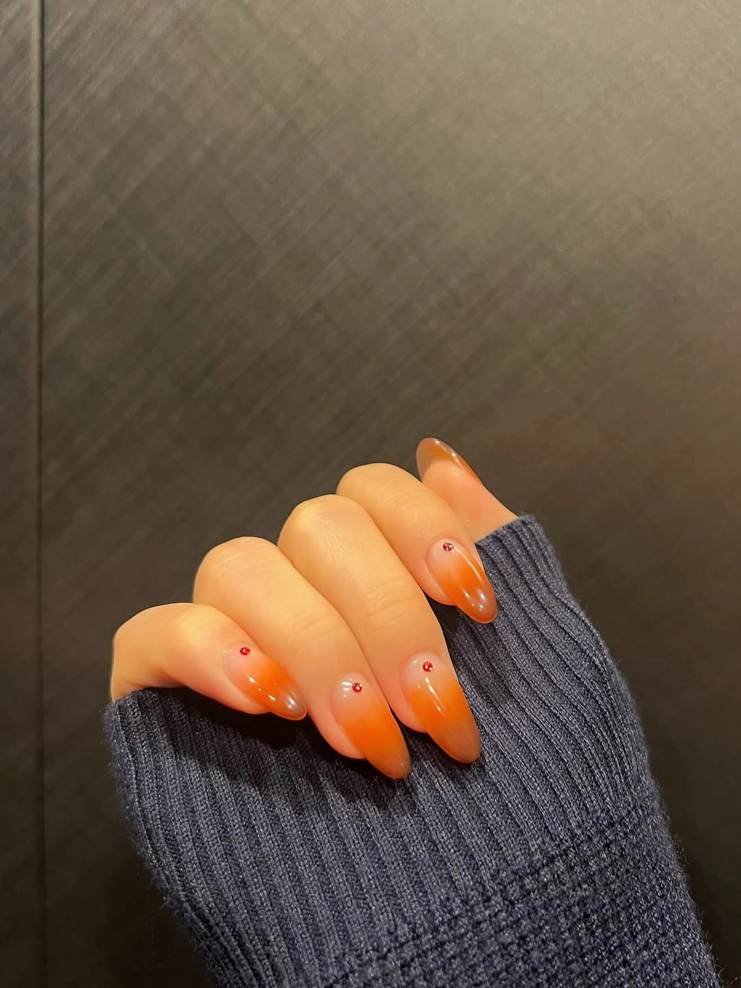 Sheer orange ombre almond nails with tiny red accents
