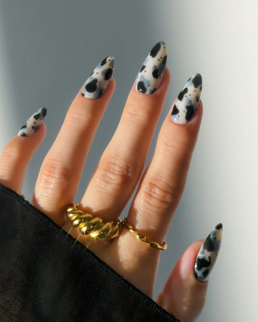 Milky almond nails covered with irregular black cow-print patches