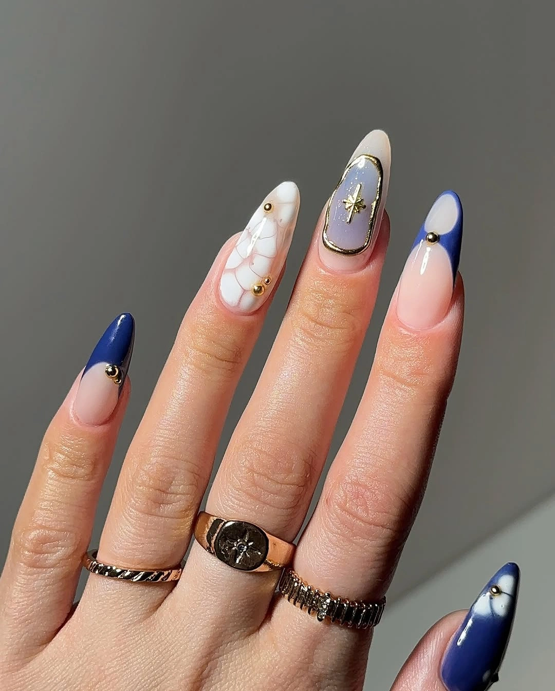 Long almond nails with milky pink bases navy tips and gold accents