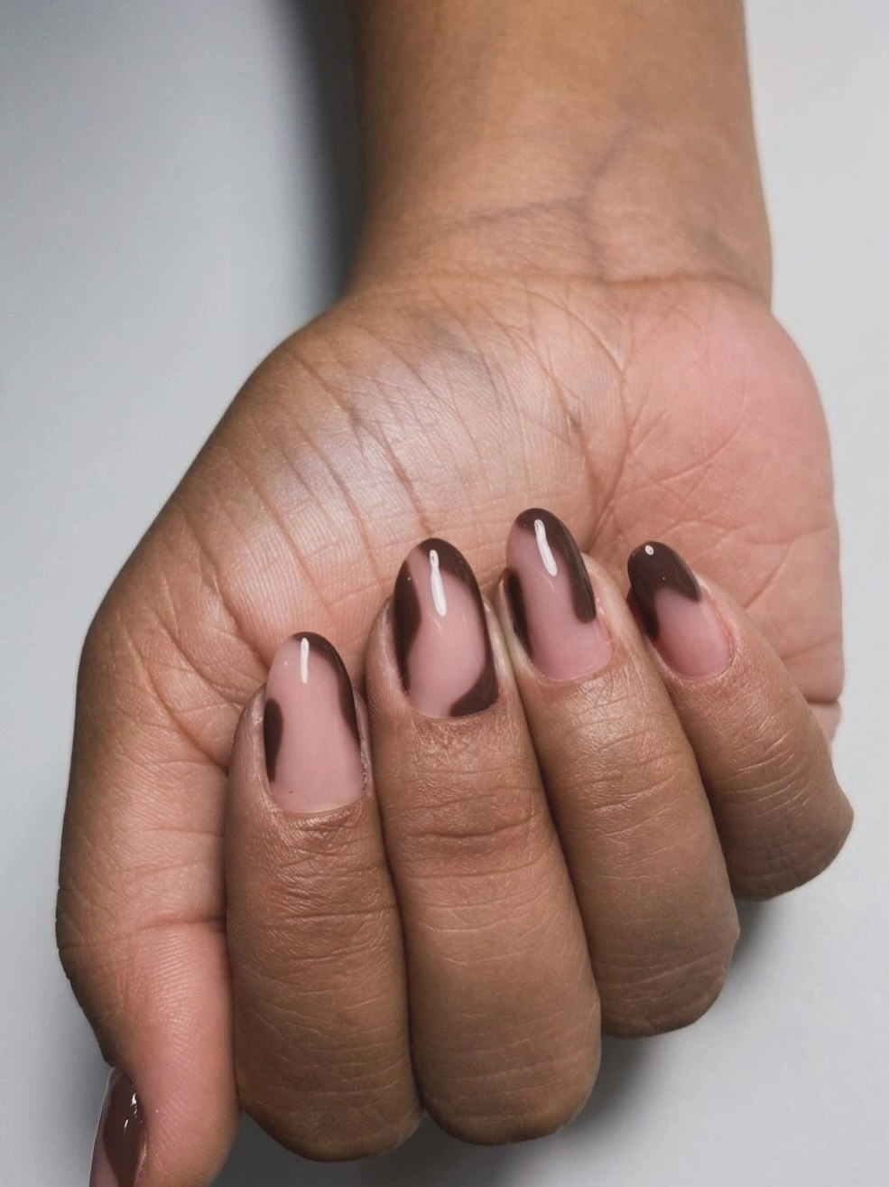 Short rounded nude nails framed with narrow glossy chocolate brown panels