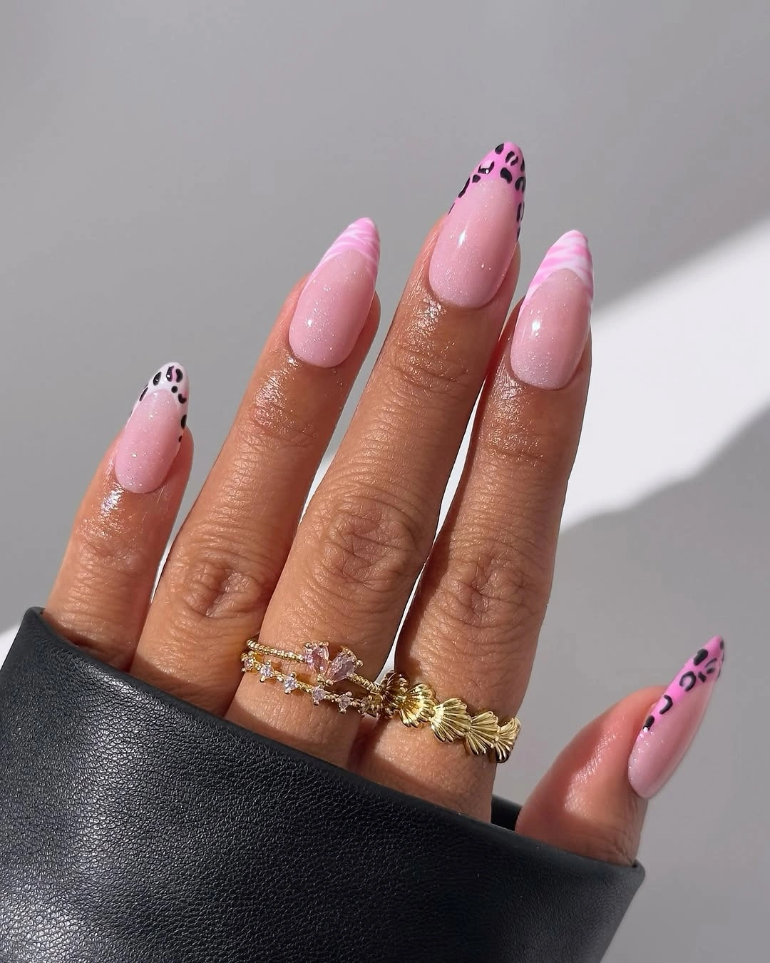 Long pink almond nails with dark spotted tips and curved accent details
