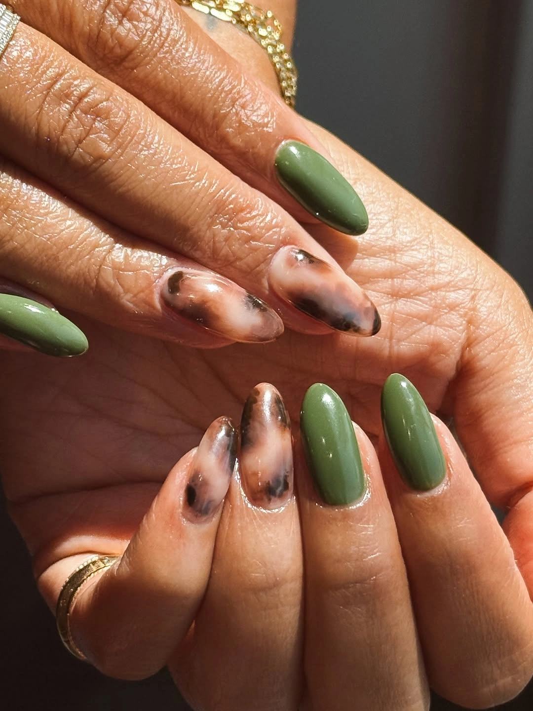 Medium almond nails alternating glossy olive green and translucent brown marbling