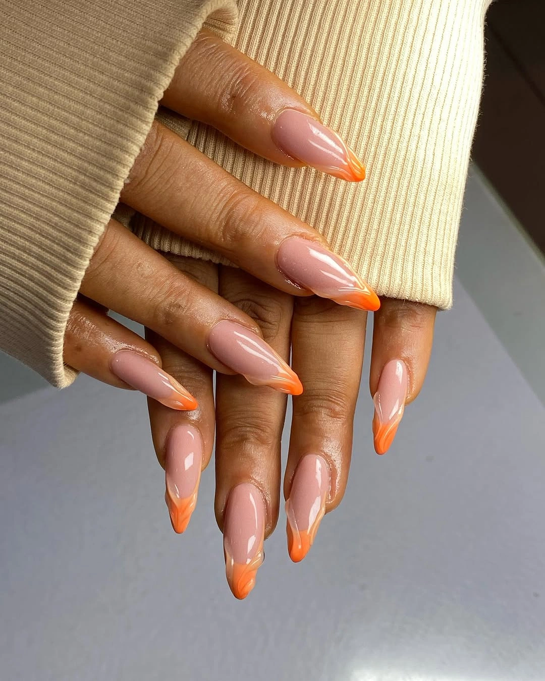 Bright orange French tips on long almond nails with nude centers