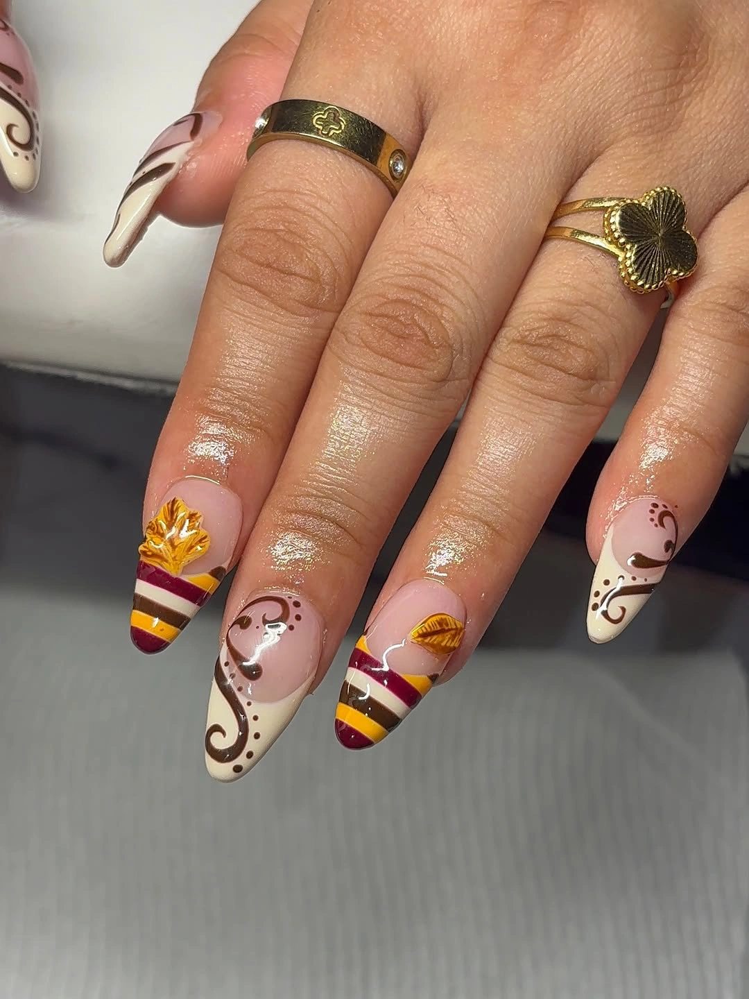 Long pale almond nails with burgundy stripes and gold curves