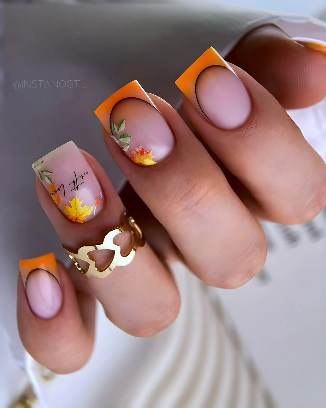 Short blush nails with bright orange tips and tiny warm accents