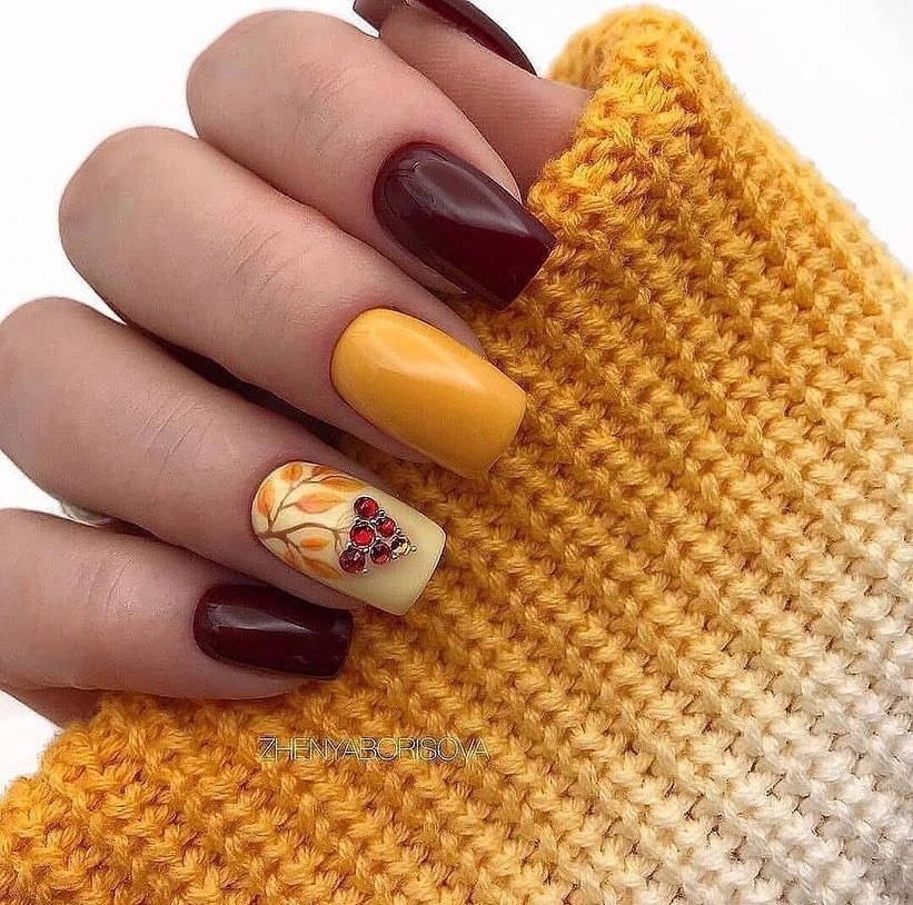 Short burgundy and mustard nails with one warm illustrated accent