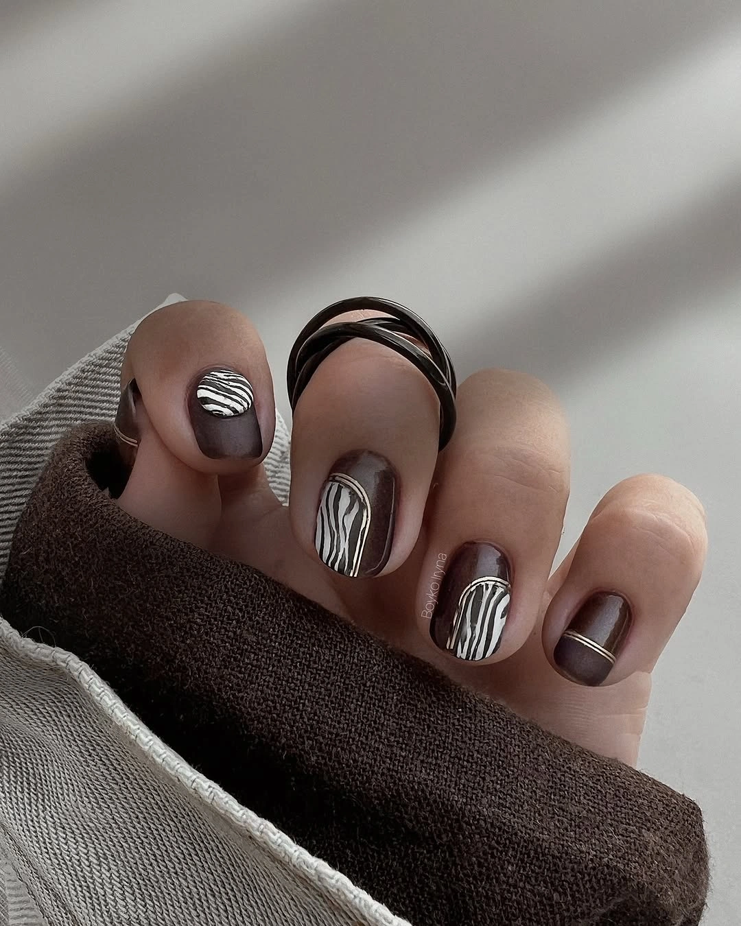 Short taupe nails with repeated black and white curved bands