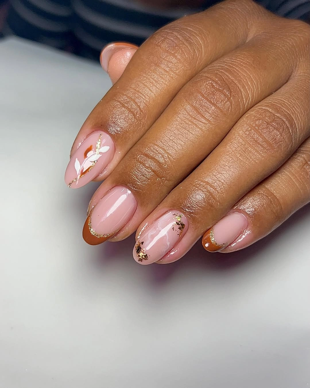 Pale pink almond nails with white floral marks and gold flecks