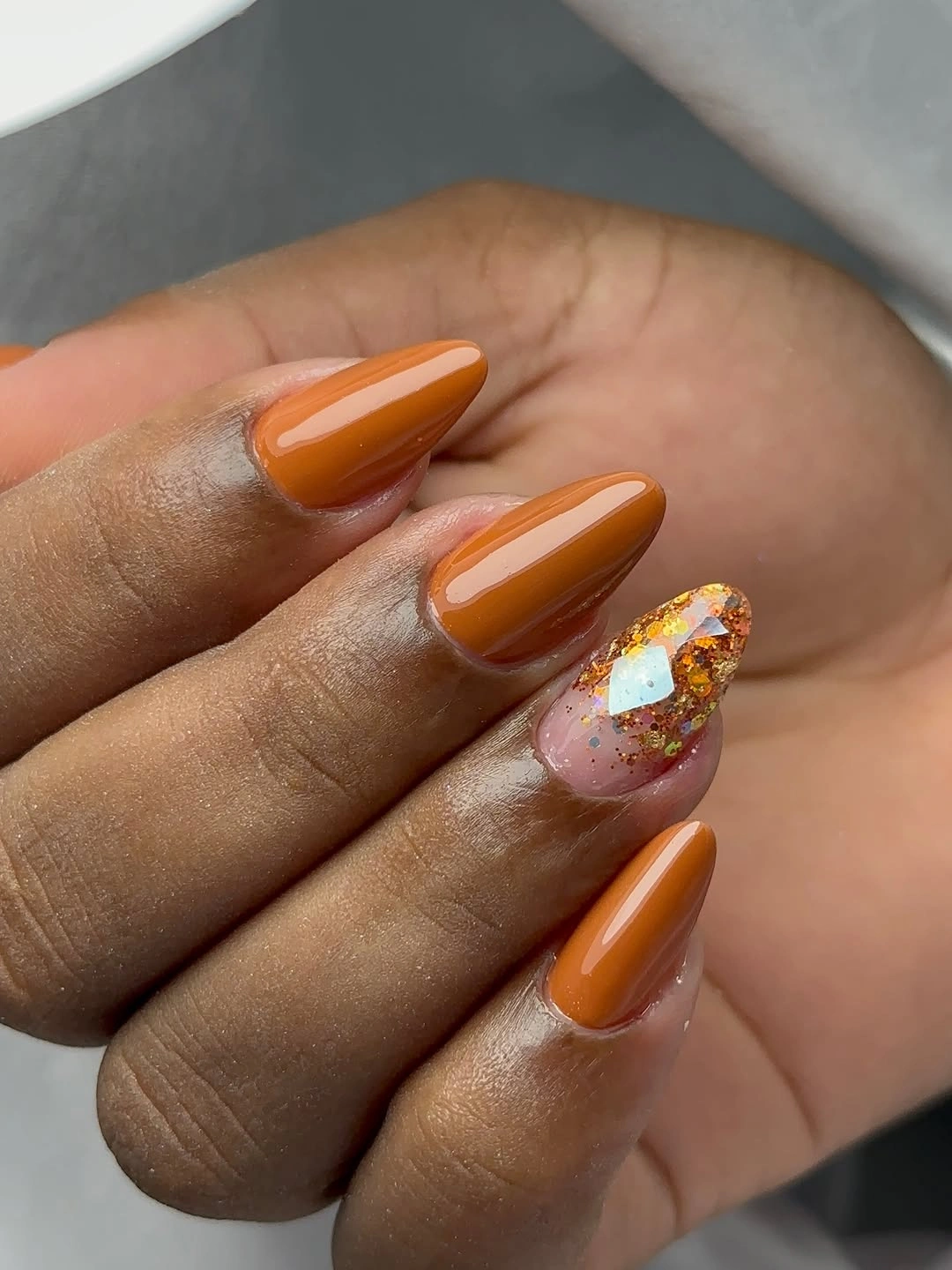 Long orange almond nails with one pale reflective accent