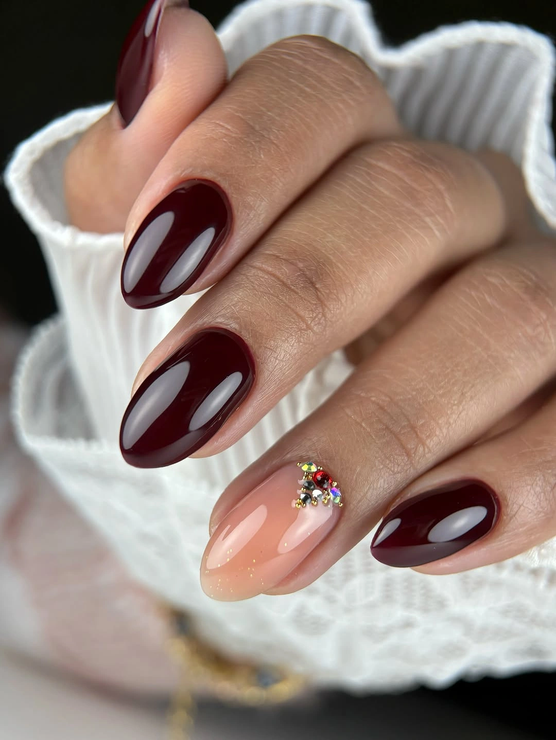 Medium burgundy almond nails with one bright clustered accent