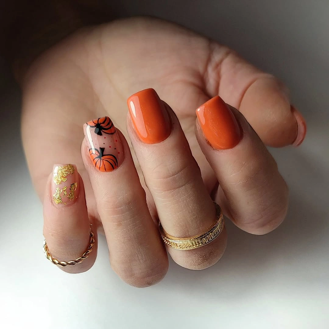 Short glossy orange nails with black pumpkin sketches and gold glitter