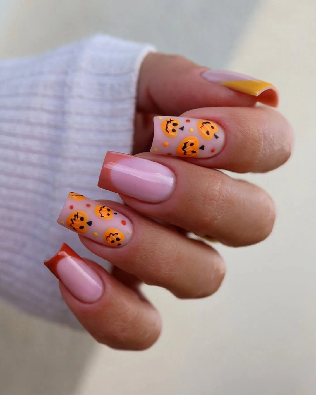Long pink square nails with orange pumpkin faces and tips
