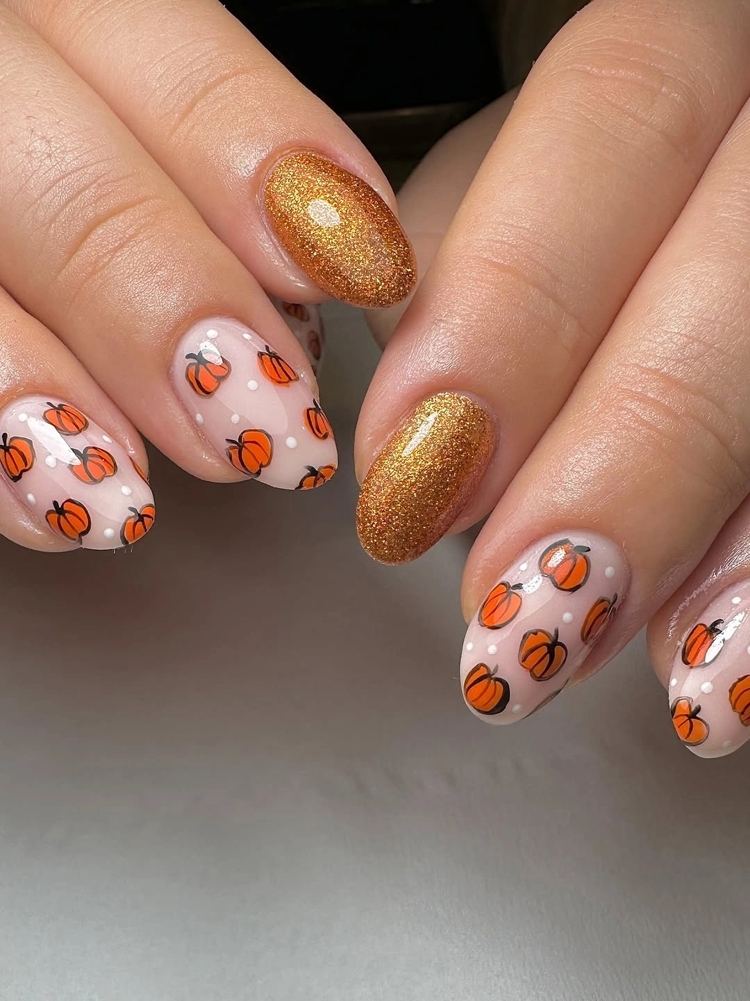 Pale pink almond nails with tiny orange pumpkins and gold shimmer