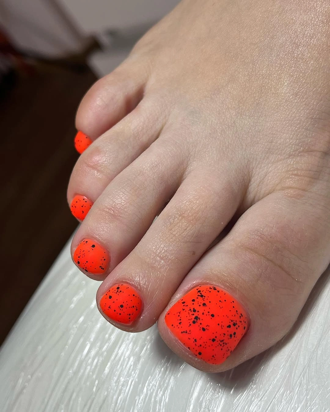 Bright orange short toenails with black speckles