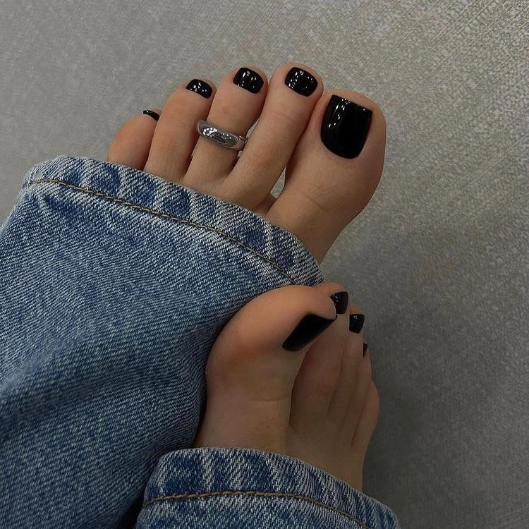 Glossy black short toenails beside blue denim