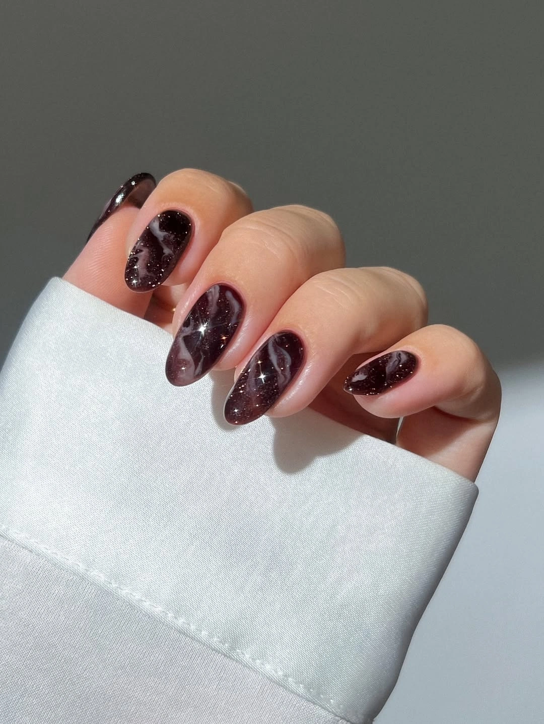 Short almond nails in chocolate burgundy with dark sparkle