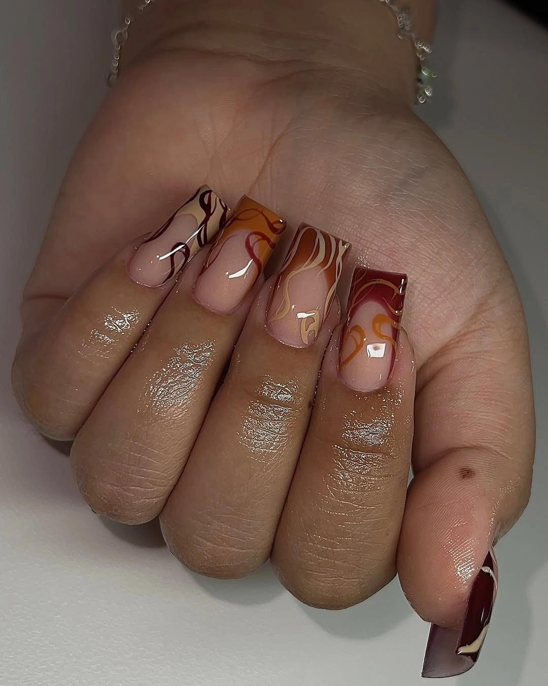 Warm brown square nails with translucent nude and wavy abstract details