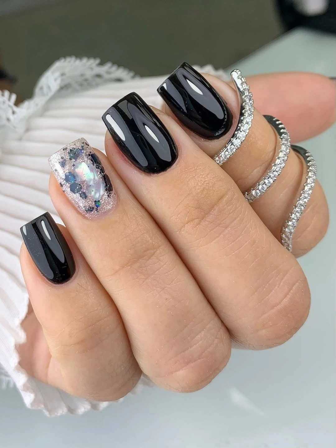 Glossy black rounded nails with one pale reflective accent
