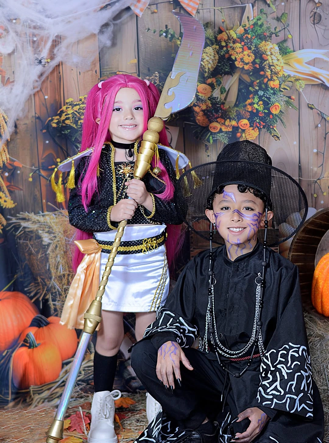 Kids Halloween duo with bright pink-haired fantasy costume and dark masked patterned outfit
