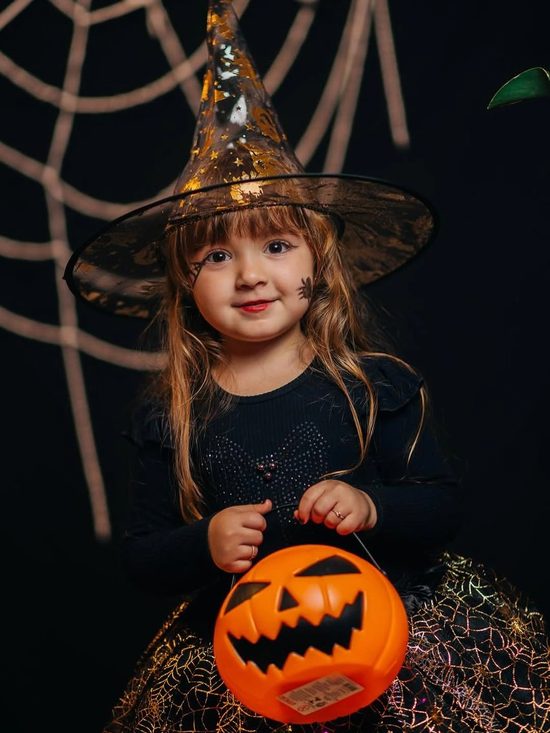 Little witch costume with black dress gold-trim pointed hat and orange pumpkin bucket