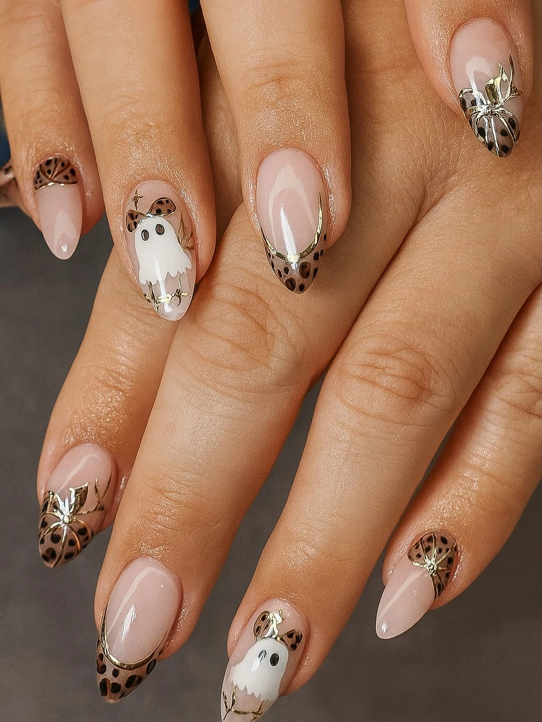Nude almond nails with white ghosts and warm patterned accents