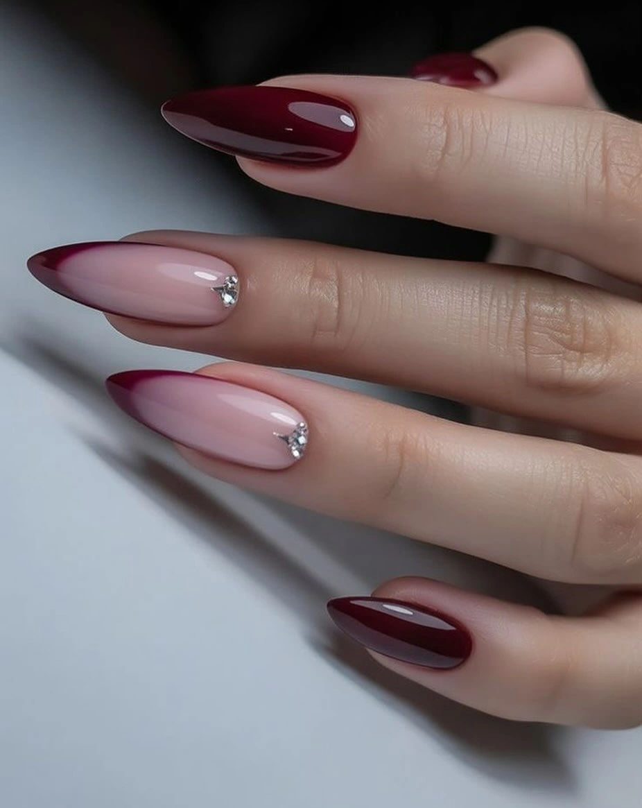 Nude almond nails with burgundy tips and clear rhinestone accents