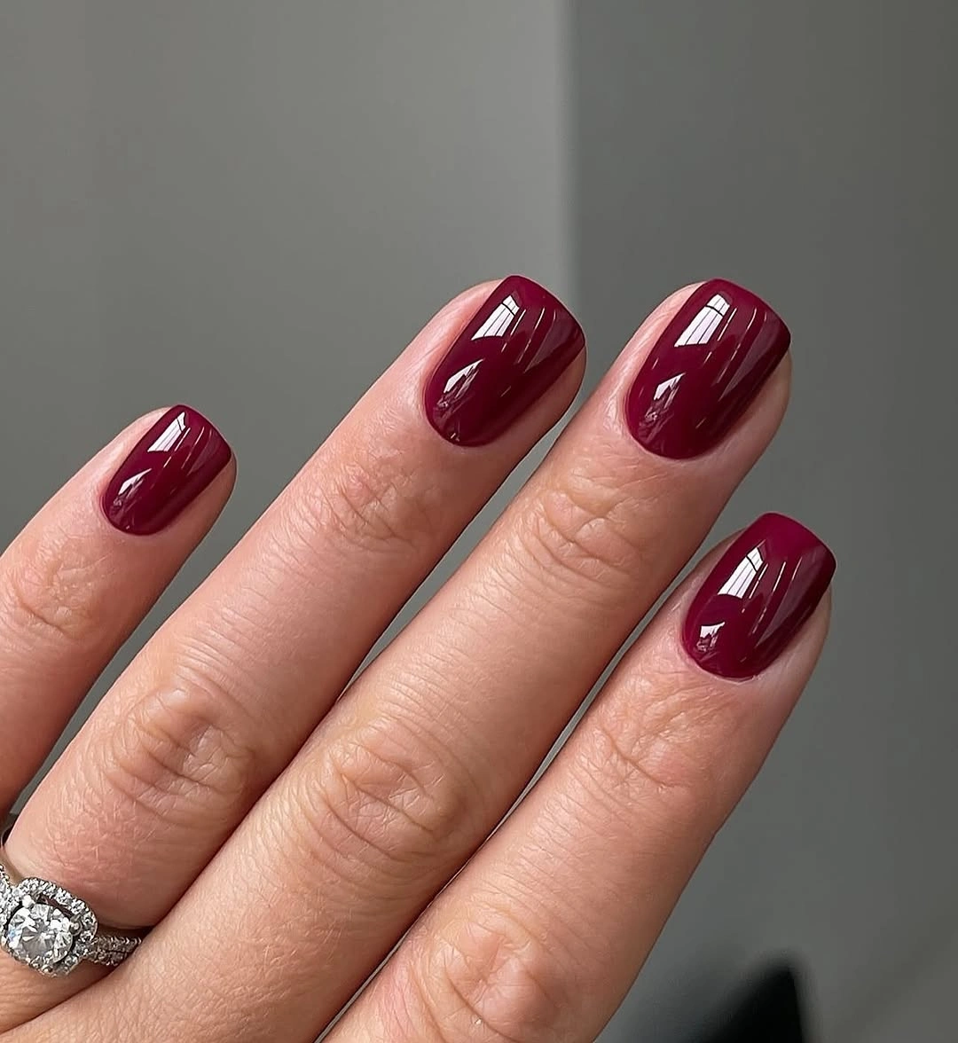 Short wine nails with subtle dark linework and small floral mark