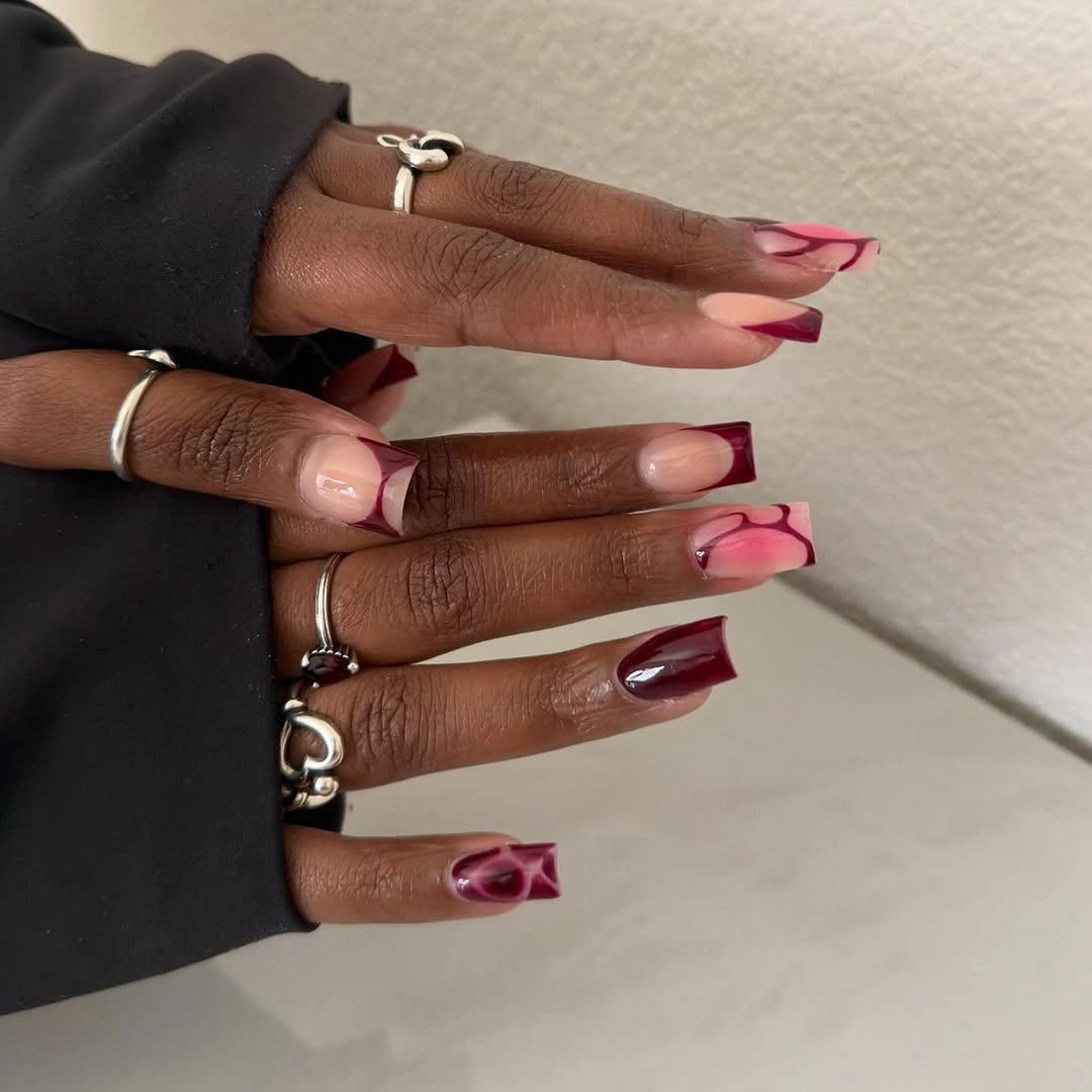 Nude square nails with varied maroon French tips and pink accent